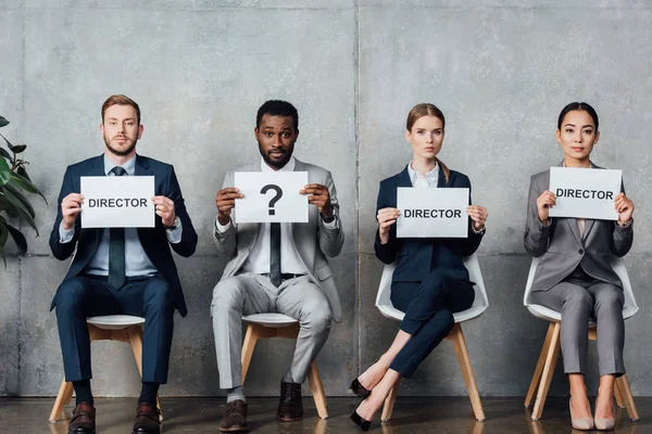 Multiethnic businesspeople holding cards with 'director' words and question mark in waiting hall — Stock Photo