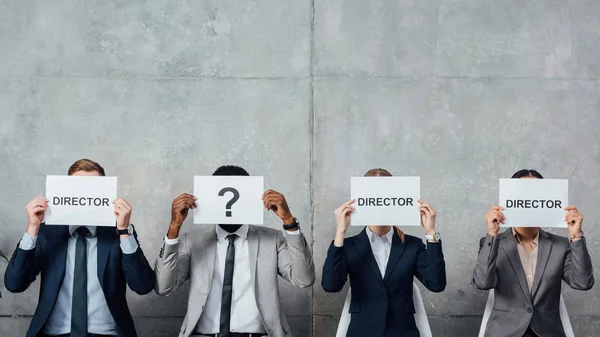 Multiethnic businesspeople holding cards with 'director' words and question mark in front of faces in waiting hall — Stock Photo