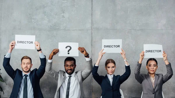 Multiethnic businesspeople holding cards with 'director' words and question mark while looking at camera — Stock Photo