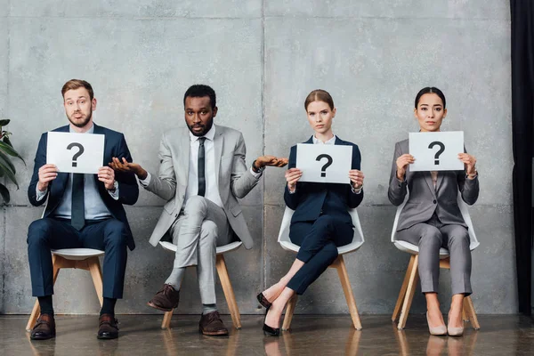 Multiethnic businesspeople holding cards with question marks in waiting hall — Stock Photo
