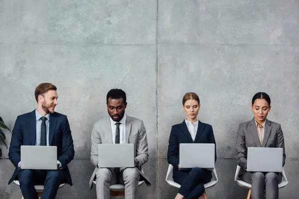 Multiethnic businesspeople sitting on chairs and using laptops in waiting hall — Stock Photo