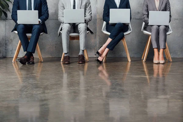 Обрезанный вид бизнесменов, сидящих на стульях и использующих ноутбуки в зале ожидания — стоковое фото