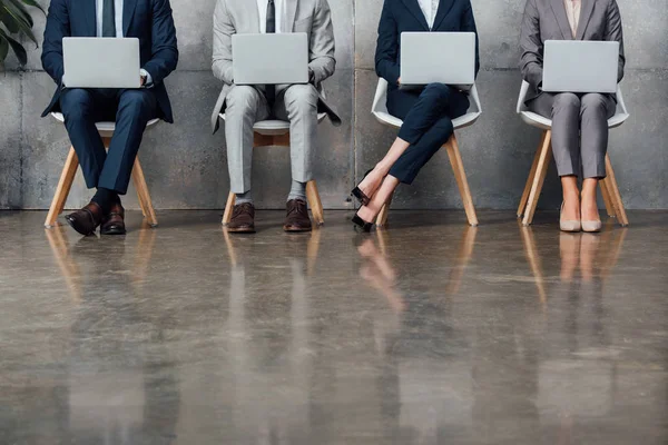 Cropped view of businesspeople sitting on chairs and using laptops in waiting hall — Stock Photo