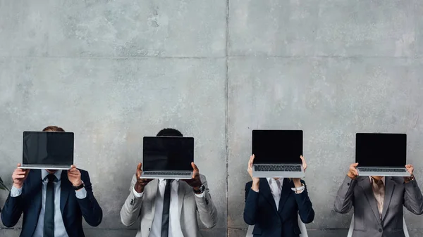 Бізнесмени сидять на стільцях і тримають ноутбуки з порожнім екраном перед обличчям в залі очікування — стокове фото