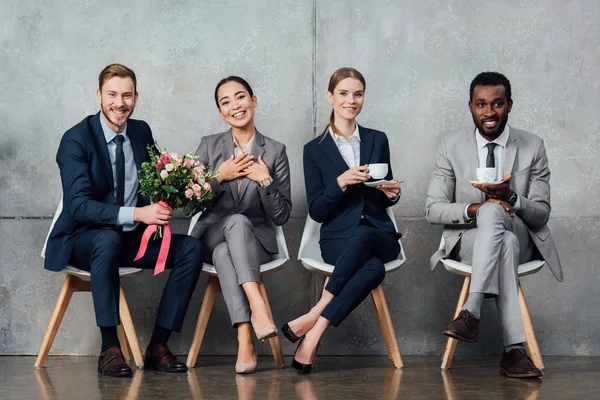 Uomini d'affari multietnici sorridenti seduti con fiori e caffè in ufficio — Foto stock