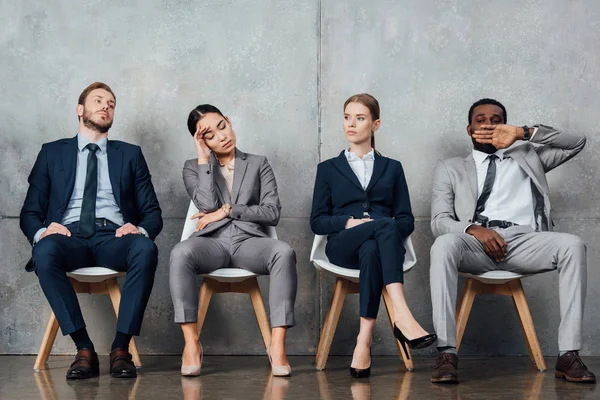 Bored multiethnic businesspeople sitting on chairs in waiting hall — Stock Photo