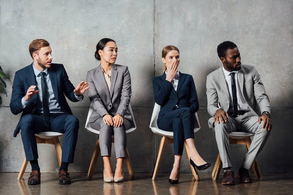 Überrascht multiethnische Geschäftsleute, die auf Stühlen sitzen und in Wartehalle wegschauen — Stockfoto