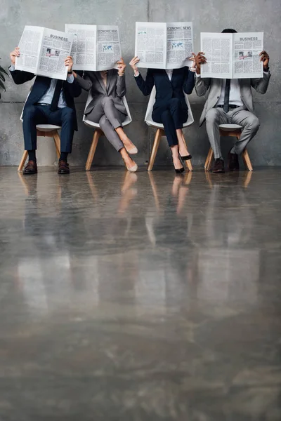 Des gens d'affaires assis sur des chaises et tenant des journaux devant des visages dans la salle d'attente avec espace de copie — Photo de stock