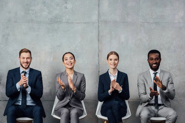 Empresarios multiétnicos sentados en sillas y aplaudiendo en la sala de espera - foto de stock