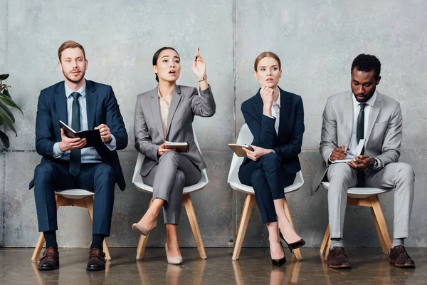 Asiático mujer de negocios levantando la mano mientras teniendo reunión con multiétnicos colegas en oficina - foto de stock