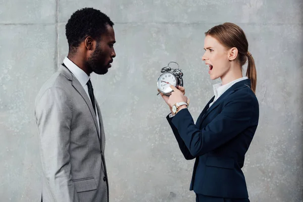 African american businessman looking at yelling businesswoman pointing at clock on grey background — Stock Photo