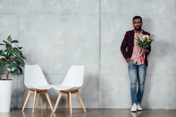 Homme afro-américain en vêtements décontractés tenant des fleurs dans la salle d'attente — Photo de stock