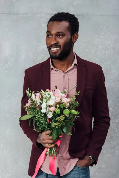 Smiling african american man in casual clothes holding flowers on grey background — Stock Photo