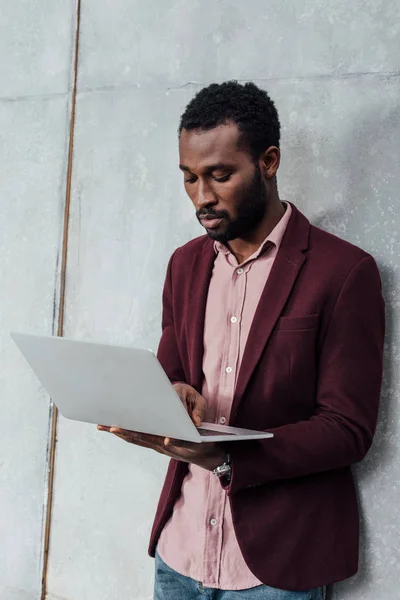 Focused african american casual businessman using laptop on grey background — Stock Photo