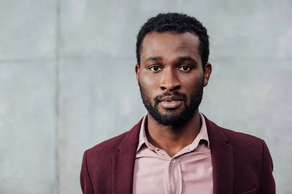 Selektiver Fokus des afrikanisch-amerikanischen Gelegenheitsunternehmers, der auf grauem Hintergrund in die Kamera blickt — Stockfoto