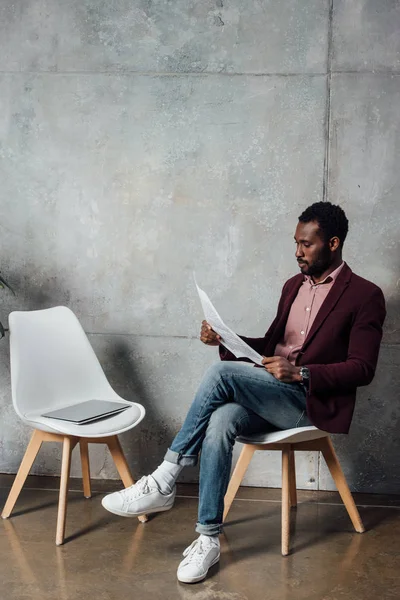 Hombre de negocios casual afroamericano sentado y leyendo el periódico en la sala de espera - foto de stock