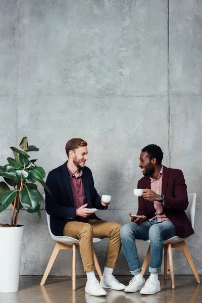 Smiling men sitting and drinking coffee while talking in waiting hall — Stock Photo