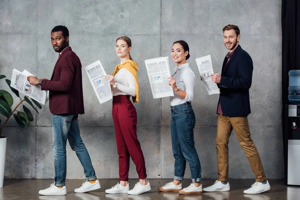 Multiethnic casual businesspeople holding newspapers and looking at camera in waiting hall — Stock Photo