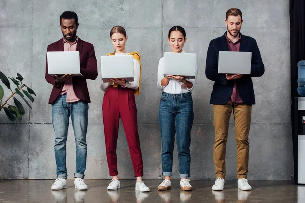 Concentrated multiethnic casual businesspeople using laptops in waiting hall — Stock Photo