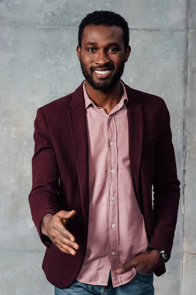 Smiling african american casual businessman outstretching hand for handshake on grey background — Stock Photo