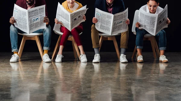 Multiethnische Gruppe von Gelegenheitsunternehmern, die auf Stühlen sitzen und Wirtschaftszeitungen lesen — Stockfoto