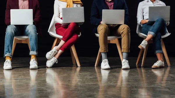 Cropped view of casual businesspeople sitting on chairs and using laptops — Stock Photo