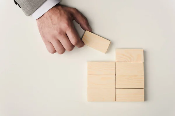 Cropped view of man holding brick in hand near wooden blocks symbolizing building success isolated on white — Stock Photo