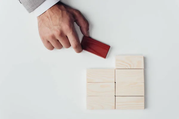 Cropped view of man holding red brick in hand near wooden blocks symbolizing building success isolated on white — Stock Photo