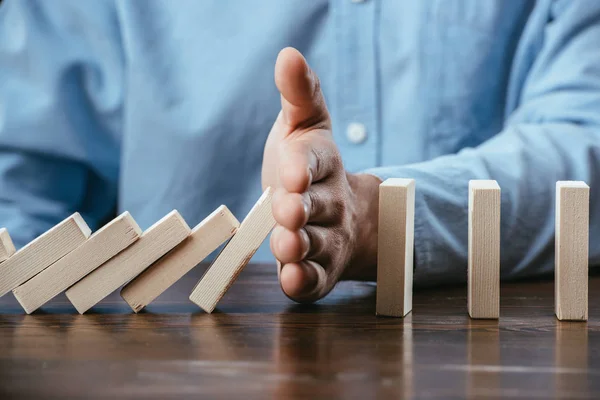 Close up view of man sitting at desk and preventing wooden blocks from falling — Stock Photo