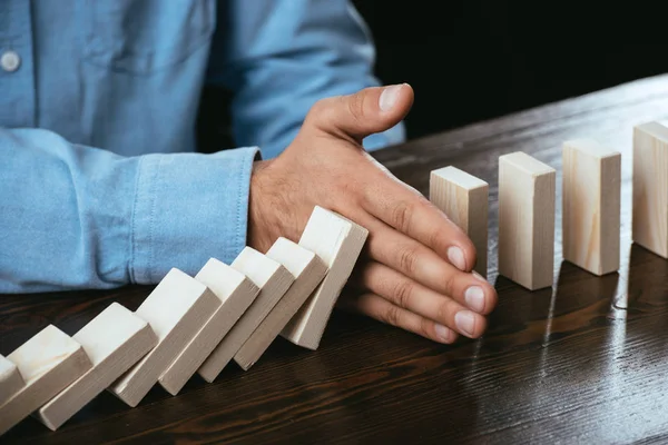 Close up view of man sitting at desk and preventing wooden blocks from falling — Stock Photo