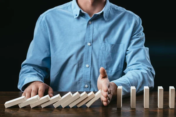 Partial view of man sitting at desk and preventing wooden blocks from falling — Stock Photo