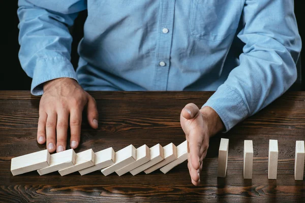 Partial view of man sitting at desk and preventing wooden blocks from falling — Stock Photo