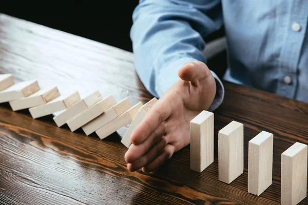 Cropped view of man sitting at desk and preventing wooden blocks from falling — Stock Photo