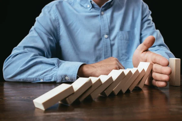 Cropped view of man sitting at desk and preventing wooden blocks from falling — Stock Photo