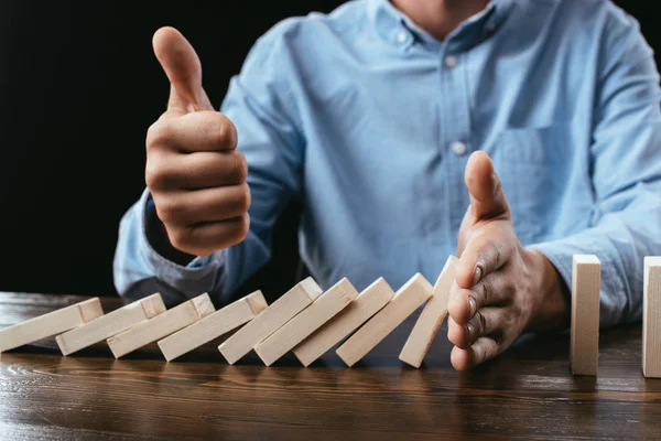 Partial view of man sitting at desk, showing thumb up sign and preventing wooden blocks from falling — Stock Photo