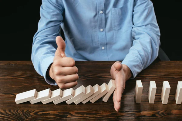 Ausgeschnittene Ansicht eines Mannes, der am Schreibtisch sitzt, Daumen hoch Zeichen zeigt und verhindert, dass Holzklötze fallen — Stockfoto