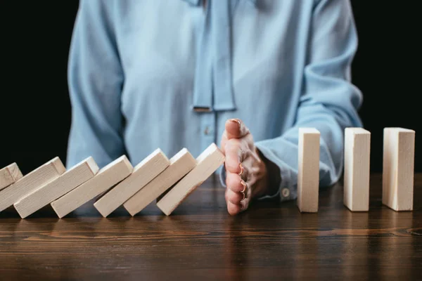 Selective focus of woman sitting at desk and preventing wooden blocks from falling with hand — Stock Photo