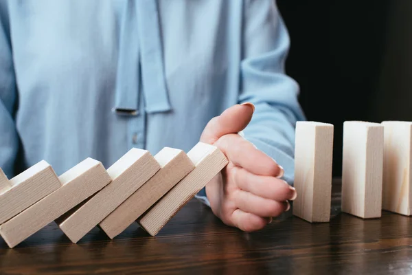 Close up view of woman sitting at desk and preventing wooden blocks from falling with hand isolated on black — Stock Photo