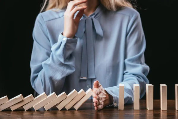 Vista recortada de la mujer en blusa azul sentada en el escritorio y evitando que los bloques de madera caigan con la mano - foto de stock