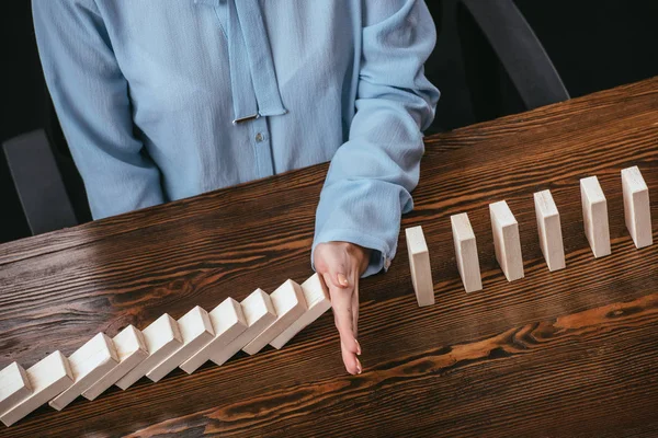 Partial view of woman in blue blouse sitting at desk and preventing wooden blocks from falling with hand — Stock Photo