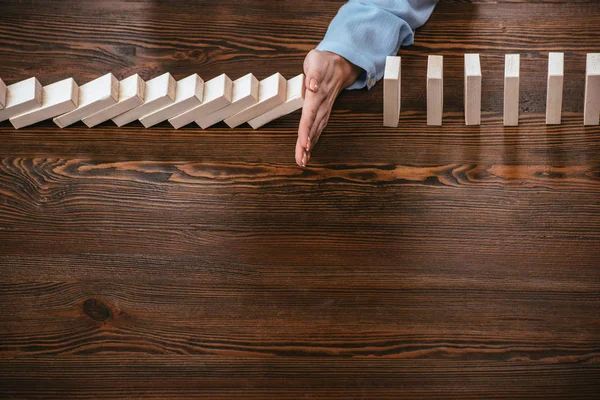 Cropped view of woman sitting at desk and preventing wooden blocks from falling with copy space — Stock Photo