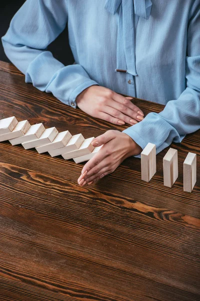 Vue partielle de la femme assise au bureau et empêchant les blocs de bois de tomber avec de l'espace de copie — Photo de stock