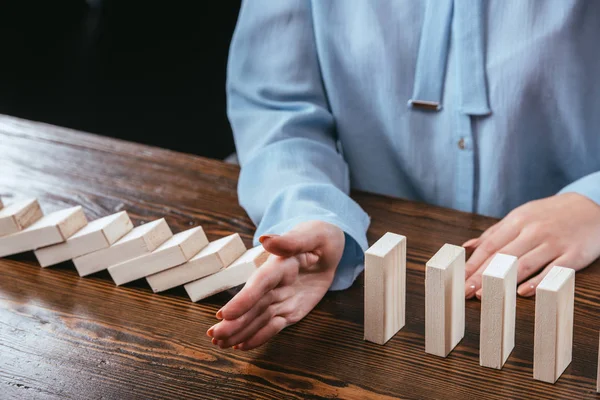 Vista parcial de la mujer sentada en el escritorio e impidiendo que los bloques de madera caigan con la mano — Stock Photo