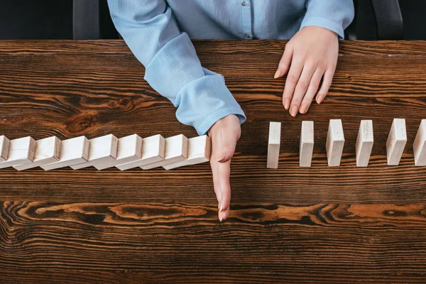 Top view of woman sitting at desk and preventing wooden blocks from falling with hand — Stock Photo