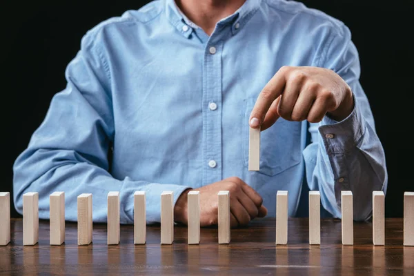 Cropped view of man picking wooden brick out of row on table isolated on black — Stock Photo