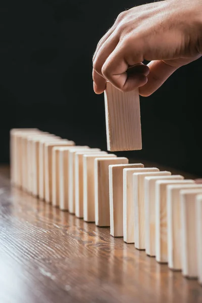 Vista de cerca del hombre recogiendo ladrillo de madera de la fila en la mesa aislado en negro — Stock Photo