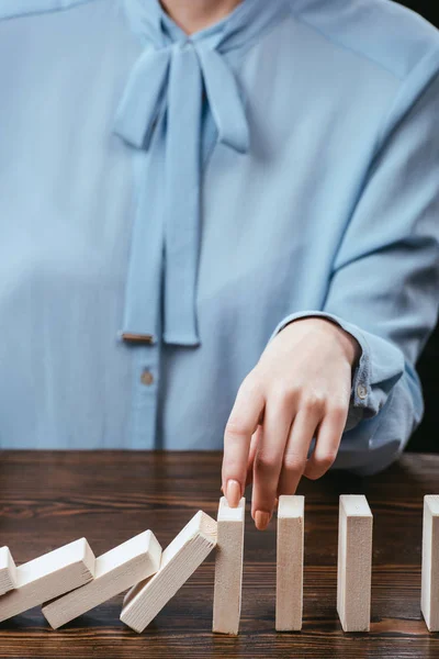 Cropped view of woman in blue blouse sitting at desk and preventing wooden blocks from falling — Stock Photo