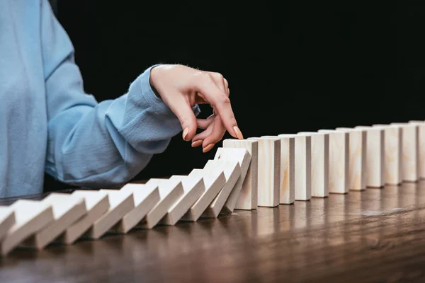 Partial view of woman preventing wooden blocks from falling isolated on black — Stock Photo