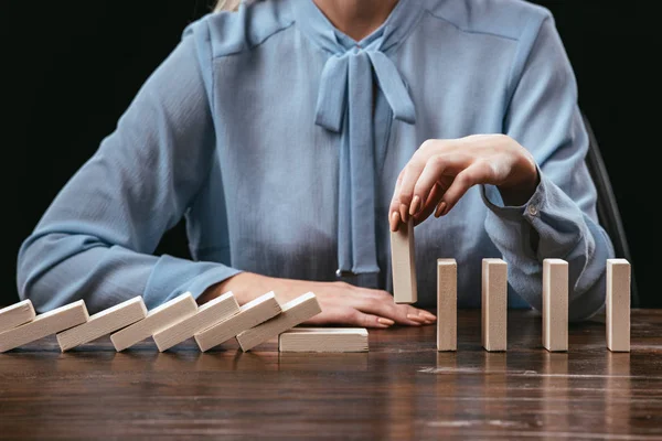 Vue partielle de la femme assise et ramassant la brique de bois de la rangée de blocs sur le bureau isolé sur noir — Photo de stock