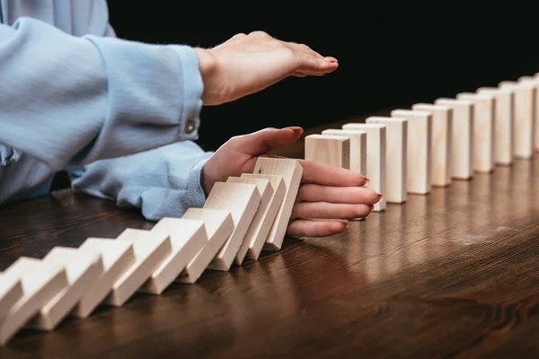 Selective focus of woman sitting at desk and preventing wooden blocks from falling isolated on black — Stock Photo